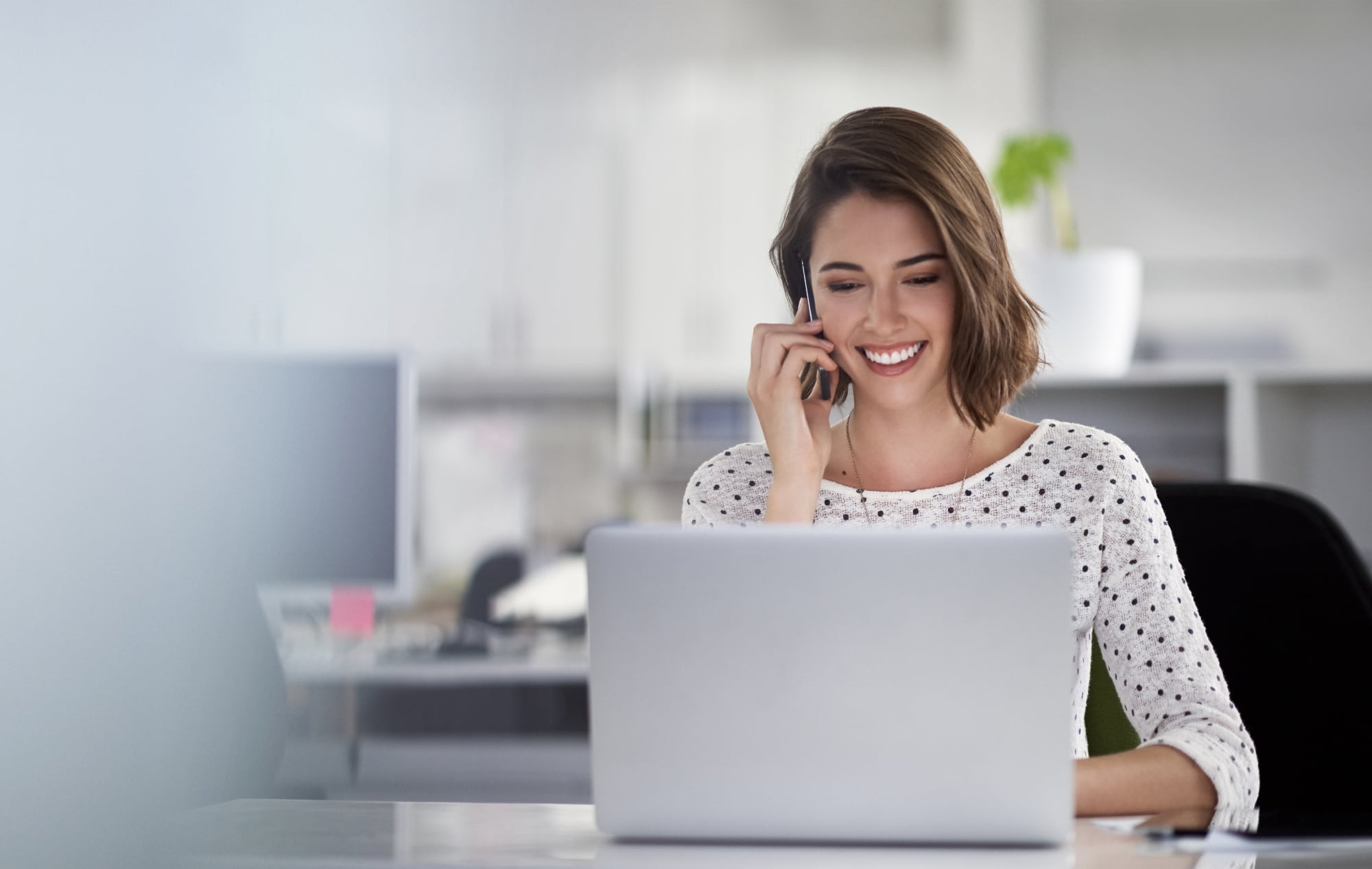 Young women talking at her mobile while using a computer.